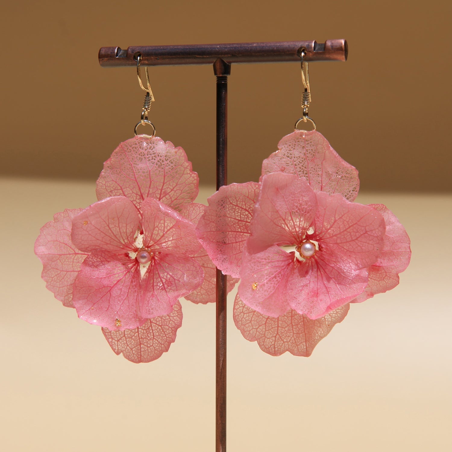 Pink floral earrings on a stand with a beige background